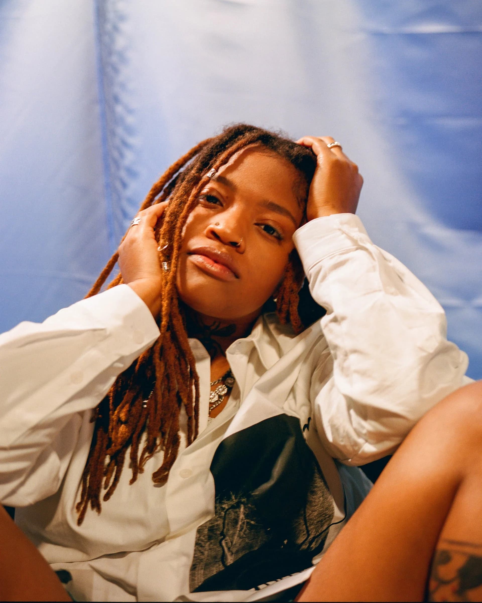 A person with long locs resting a hand near their head